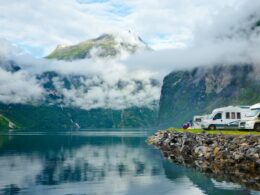 A row of motorhomes parked along an embankment of a turqoise lake and mountain range.