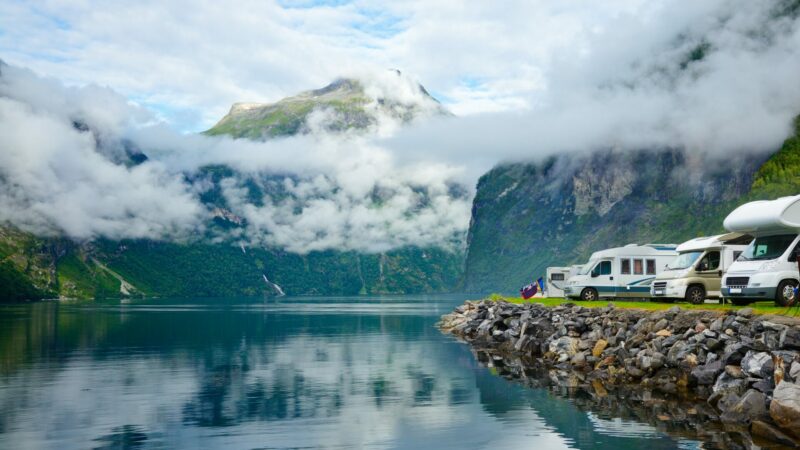 A row of motorhomes parked along an embankment of a turqoise lake and mountain range.