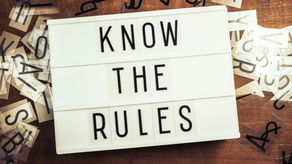 A letterboard that states "Know the Rules" with letters scattered behind it on a wooden table. 