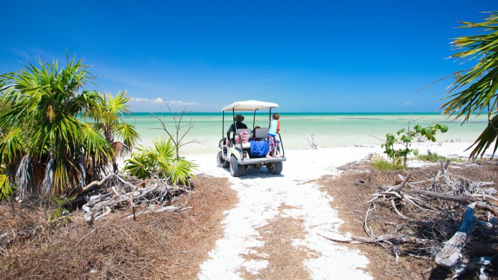 A person and their child on a golf cart as they drive to the beach. 