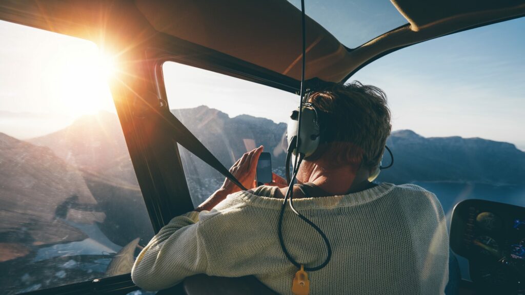 A person taking a photo with their cellphone from the inside of a helicopter. 