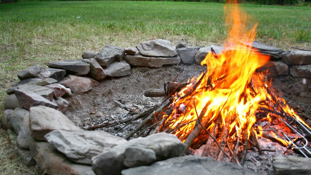 A fire pit with a rocky border and green grass surround it. 