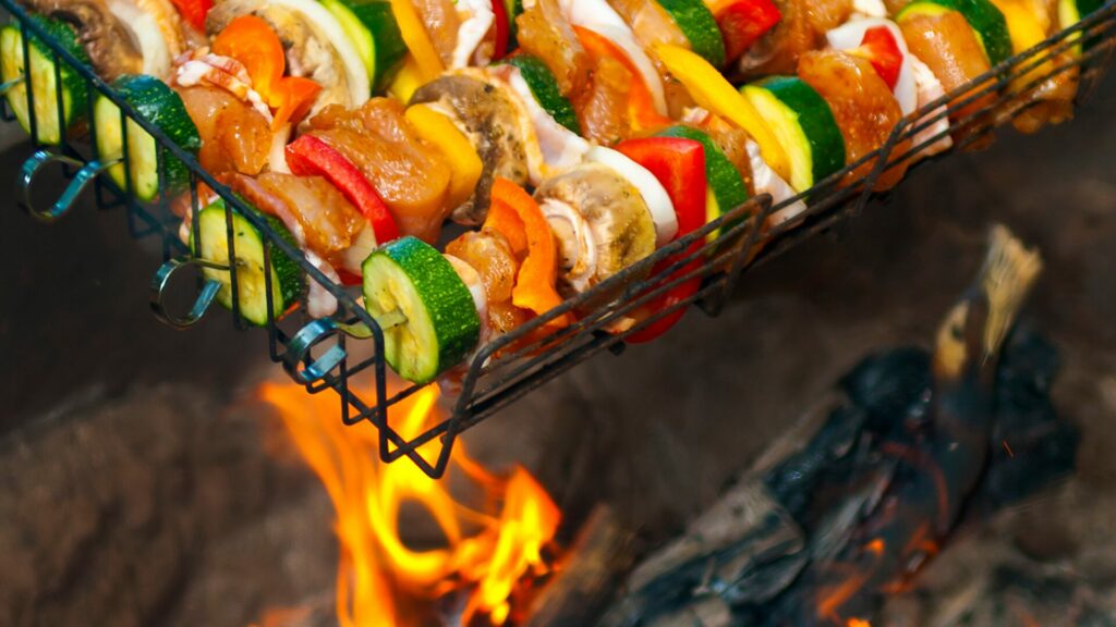 Skewers of meat and vegetables in a holding grate above an open fire. 