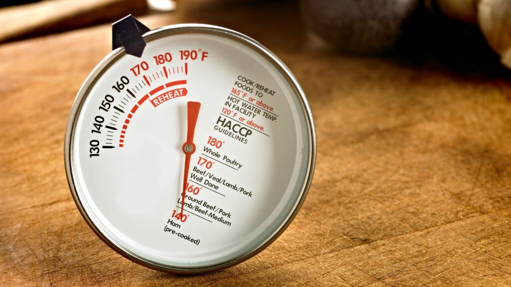 A meat thermometer sitting atop a cutting board with HACCP guidelines printed on it.