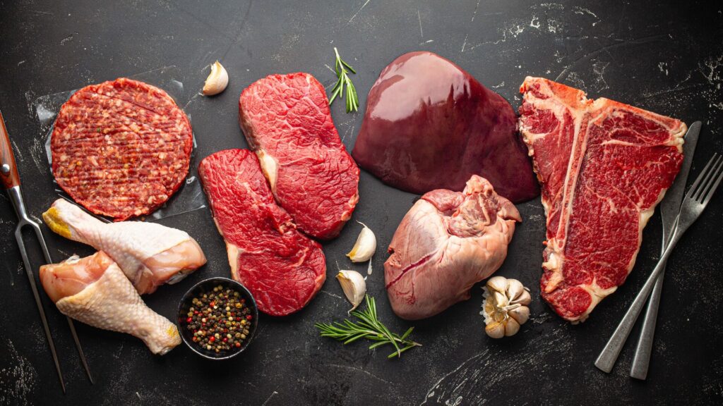 Assorted meats, herbs, and seasonings atop a black marble surface with cooking and dining utensils. 