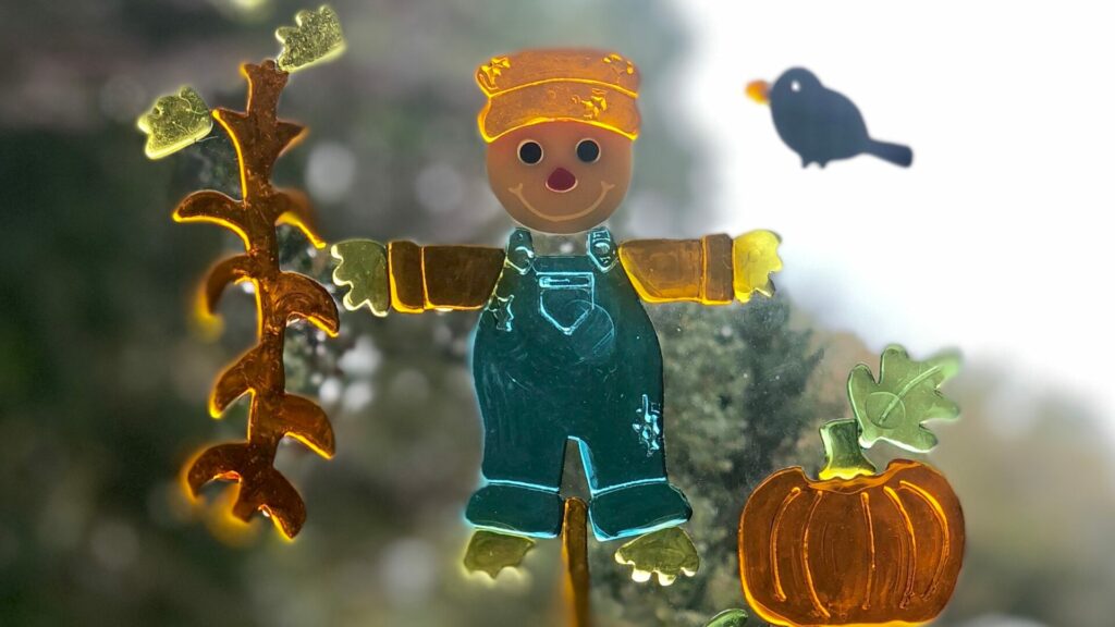 A scarecrow, crow, corn stalk, and pumpkin window cling stuck to a window. 