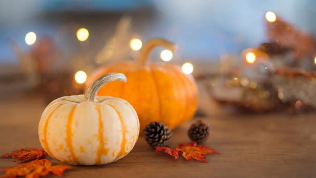 Mini pumpkins, faux orange maple leaves, fairy lights, and small pinecones adorn a counter top for fall decorations. 