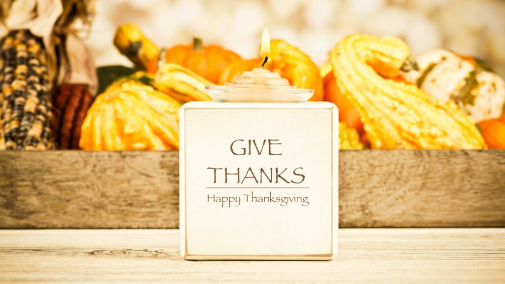 A basket of gourds and corn behind a Give Thanks Happy Thanksgiving sign. 