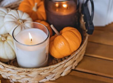 A basket with lit candles and mini pumpkins.