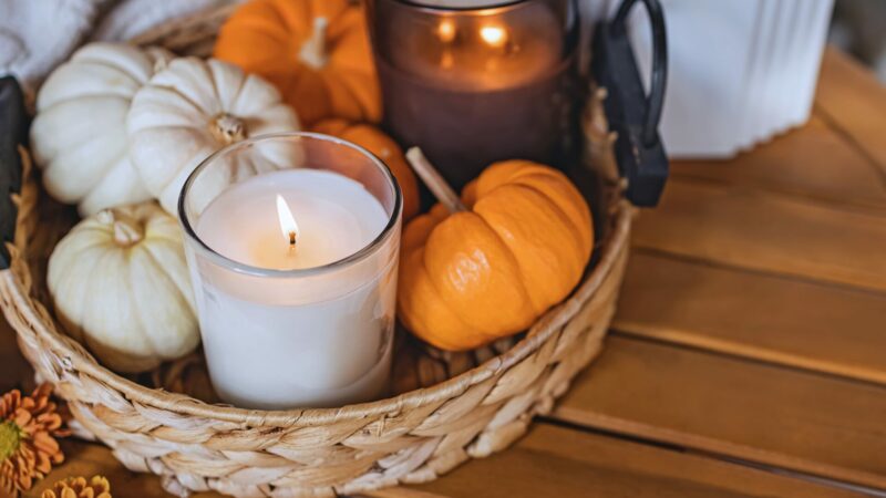 A basket with lit candles and mini pumpkins.