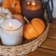 A basket with lit candles and mini pumpkins.