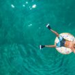 Person in donut pool innertube with flippers on their feet and goggles on their head as they float atop the water.