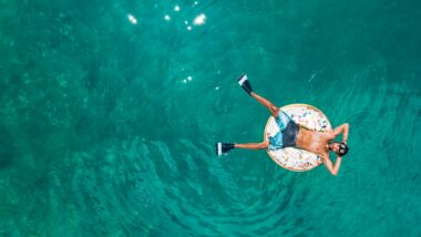 Person in donut pool innertube with flippers on their feet and goggles on their head as they float atop the water.