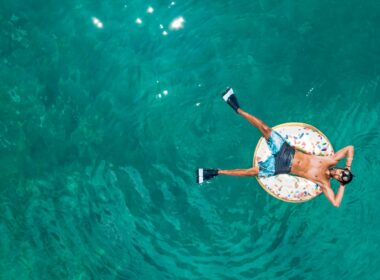 Person in donut pool innertube with flippers on their feet and goggles on their head as they float atop the water.