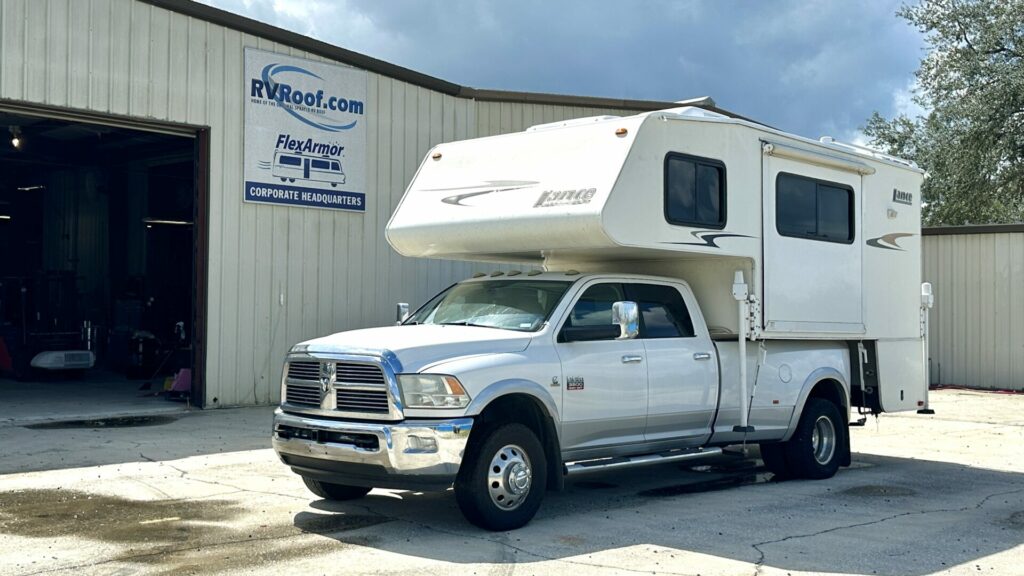 A camper installed atop the bed of a Dodge Ram Truck sitting in front of the RV FlexArmor building. 