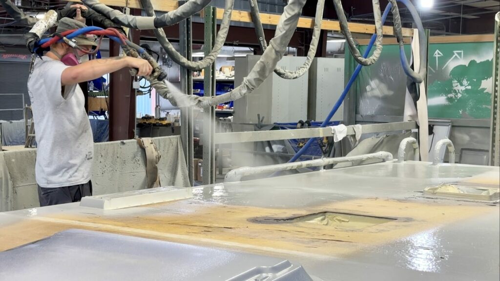 A person spraying the roof of the Getaway Couple's RV with RV FlexArmor as hosing hangs from the ceiling behind the person. 