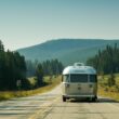 An Airstream Travel Trailer being towed down a road lined with fir and pine trees.