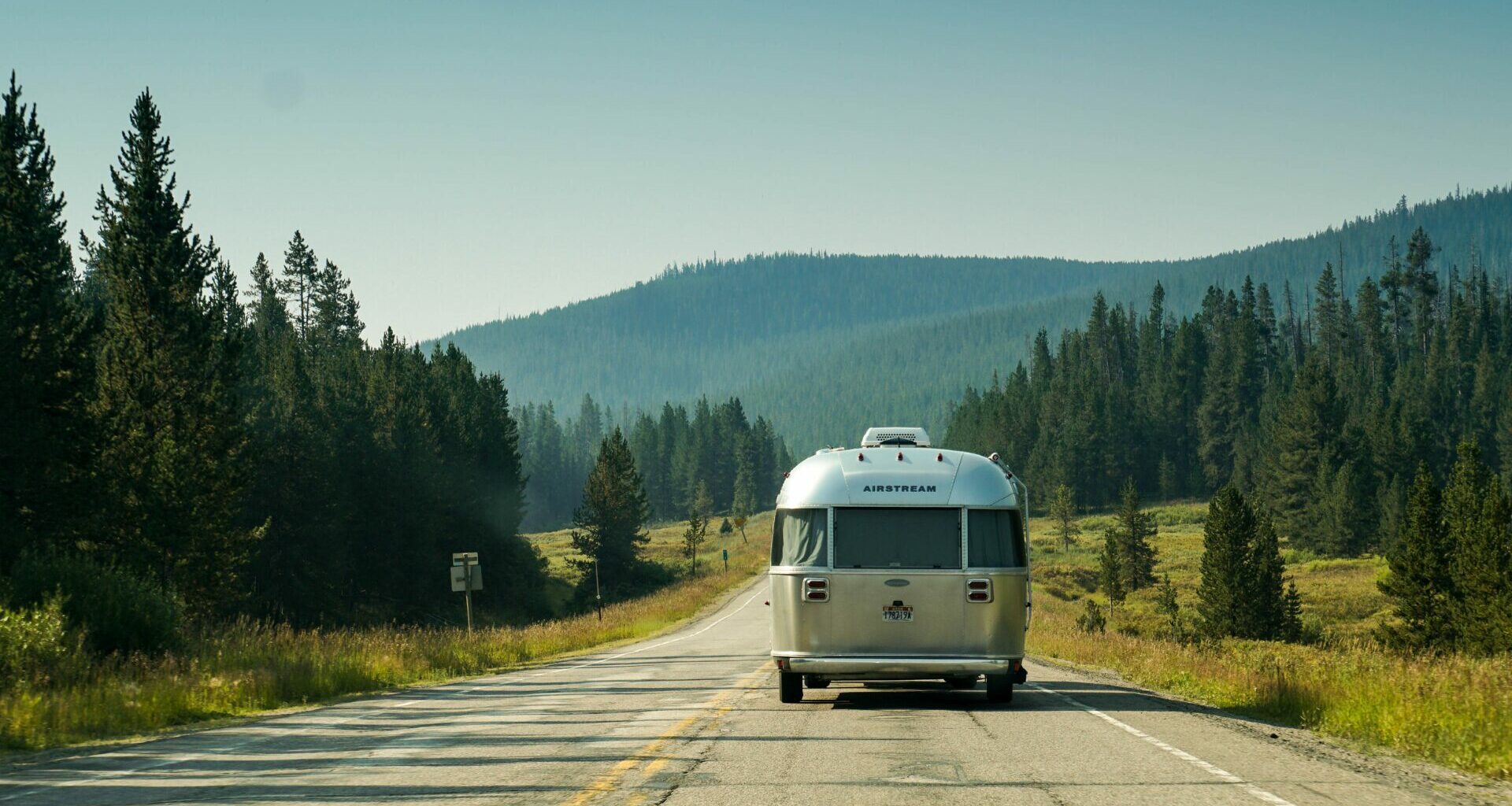 An Airstream Travel Trailer being towed down a road lined with fir and pine trees.