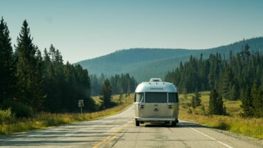 An Airstream Travel Trailer being towed down a road lined with fir and pine trees.