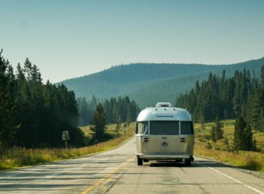 An Airstream Travel Trailer being towed down a road lined with fir and pine trees.