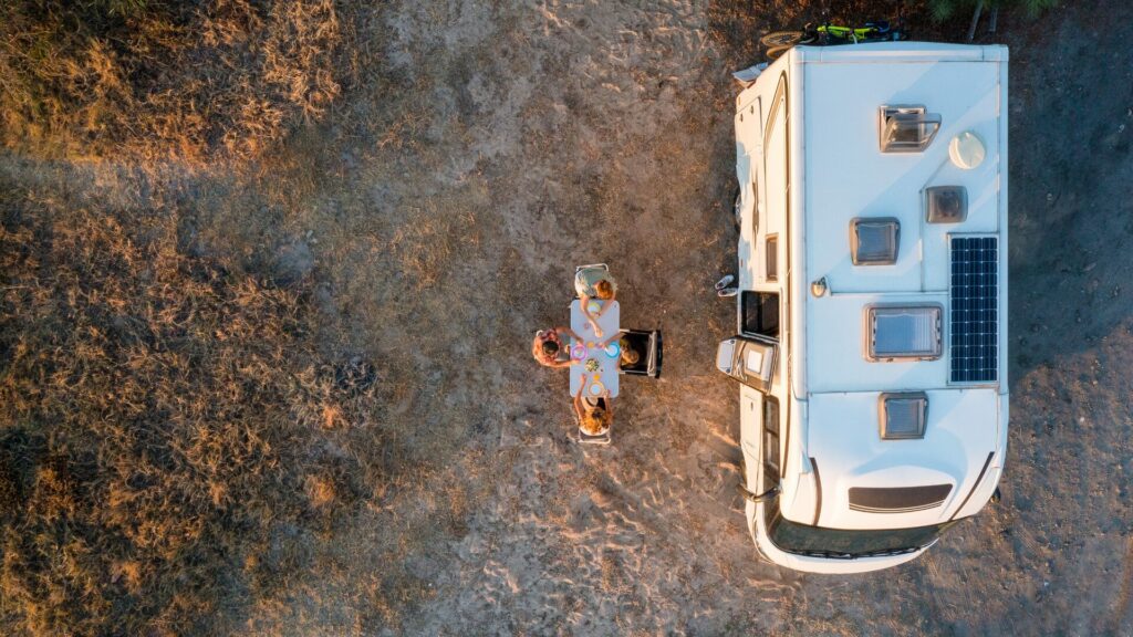 An aerial photo of four people sat around a table beside their motorhome outdoors.