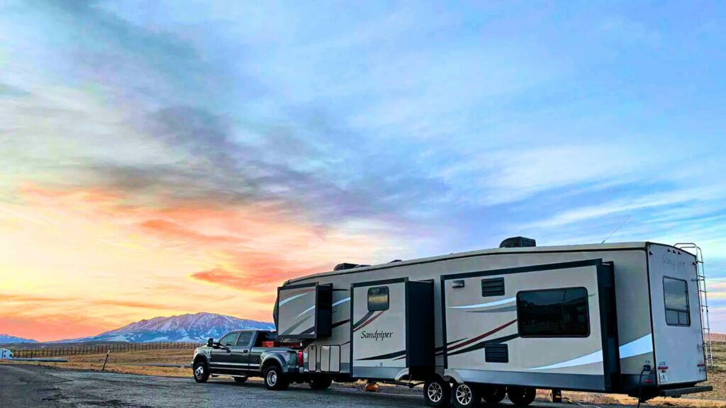 A Forest River RV travel trailer hitched up to a truck on the side of a road with a sunset sky behind it. 