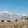 A lineup of six Winnebago travel vans in front of a mountain range.