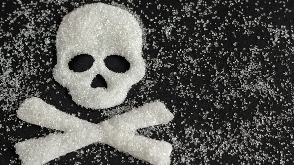 Sugar dispersed and collected into the shape of skull and crossbones apon a black background. 