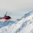 An aerial photo of a red Whistler Helicopter Tour Helicopter flying over snowy mountains.