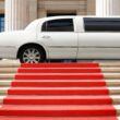 A white limo parked in front of a red capret that is rolled out over a set of stairs.