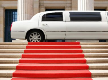 A white limo parked in front of a red capret that is rolled out over a set of stairs.