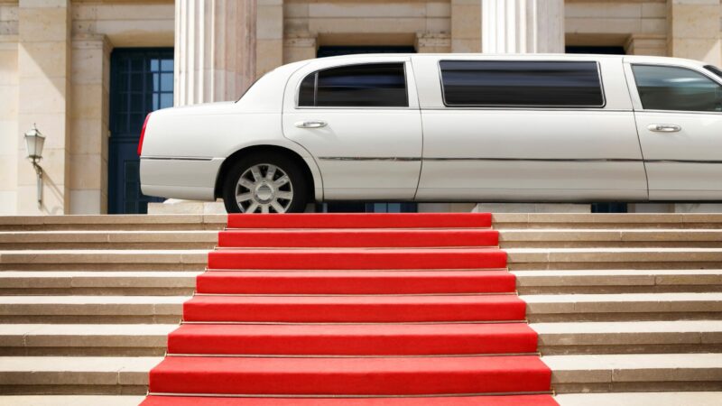 A white limo parked in front of a red capret that is rolled out over a set of stairs.