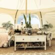 A glamping tent set up with a dressing table, bed, plants, and other decor.