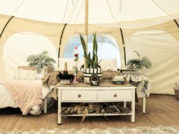 A glamping tent set up with a dressing table, bed, plants, and other decor.