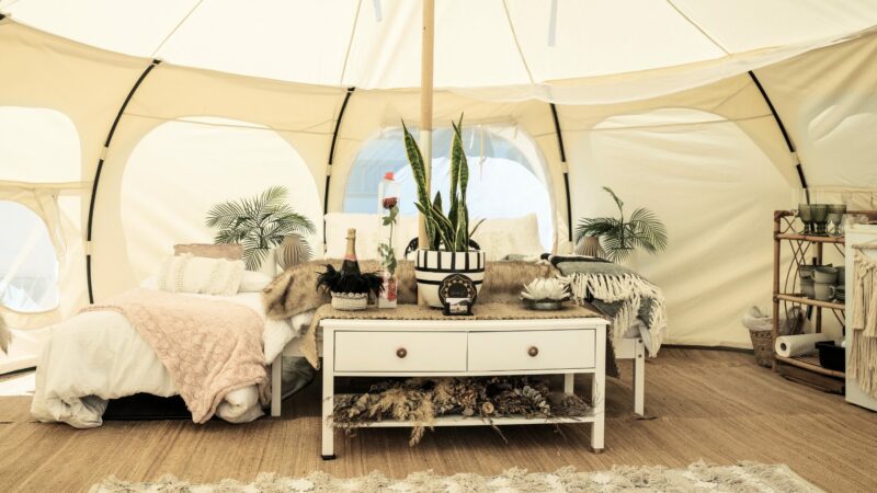 A glamping tent set up with a dressing table, bed, plants, and other decor.