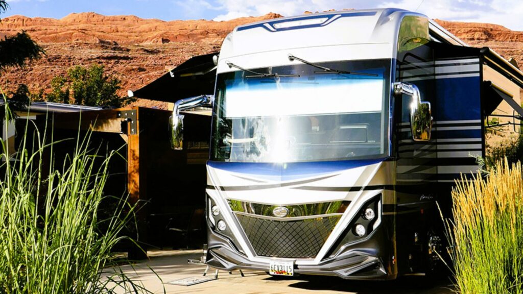 One of American Coach's motorhomes set up at a RV park with red rocky cliffs in the background.