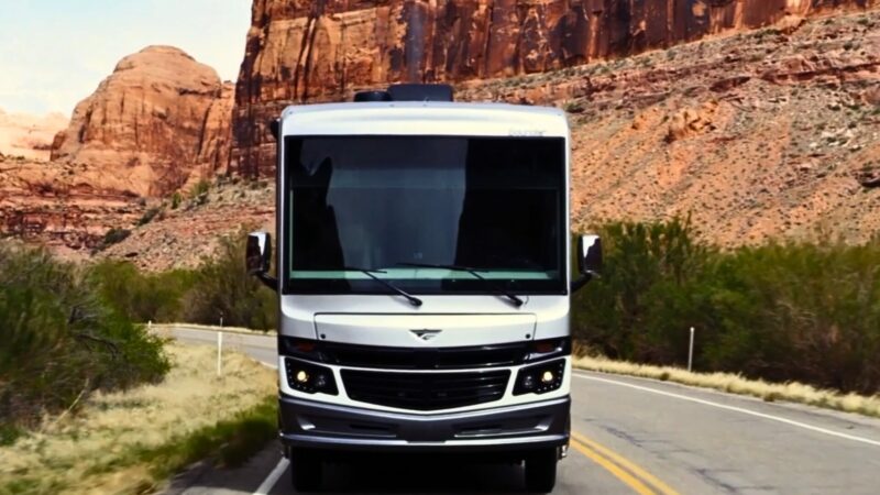 One of REV Group's motorhomes driving through a red rocky desert landscape on a road.