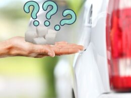 Hand holding sugar cubes beside a gas tank opening of a car with three blue question marks above it.