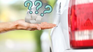 Hand holding sugar cubes beside a gas tank opening of a car with three blue question marks above it.