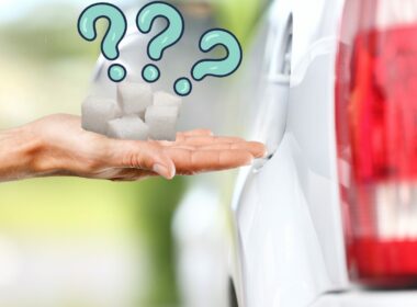 Hand holding sugar cubes beside a gas tank opening of a car with three blue question marks above it.