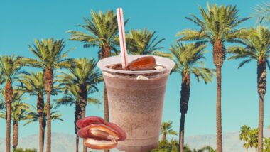 A shake with dates upon and beside it as it sits in front of a photo of date trees side by side with a bright blue background.